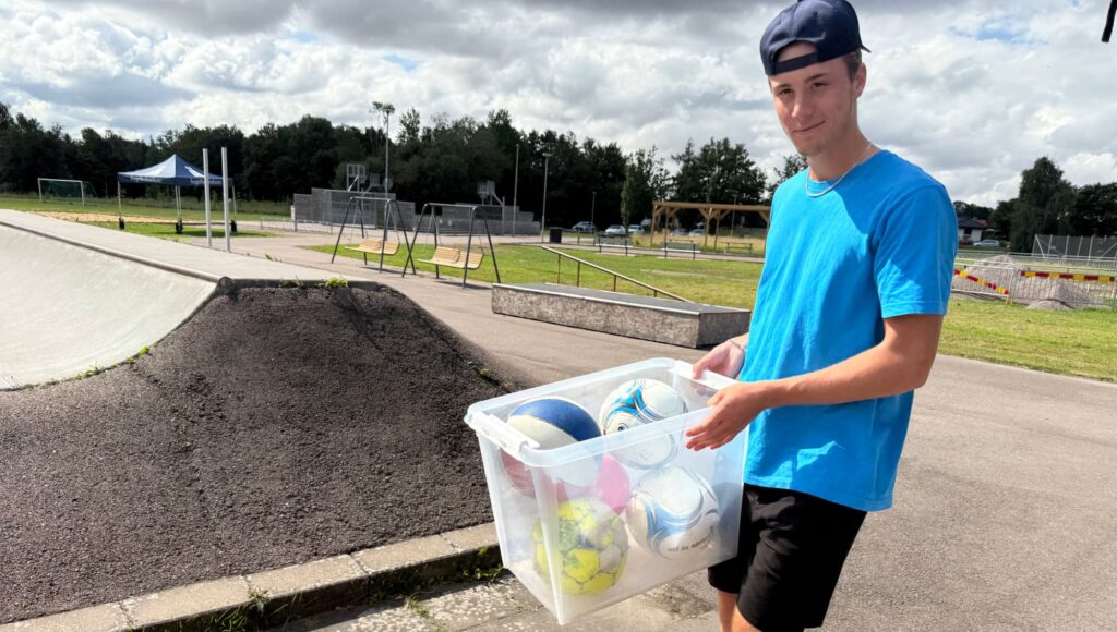 En ung kille i keps håller en låda med fotbollar