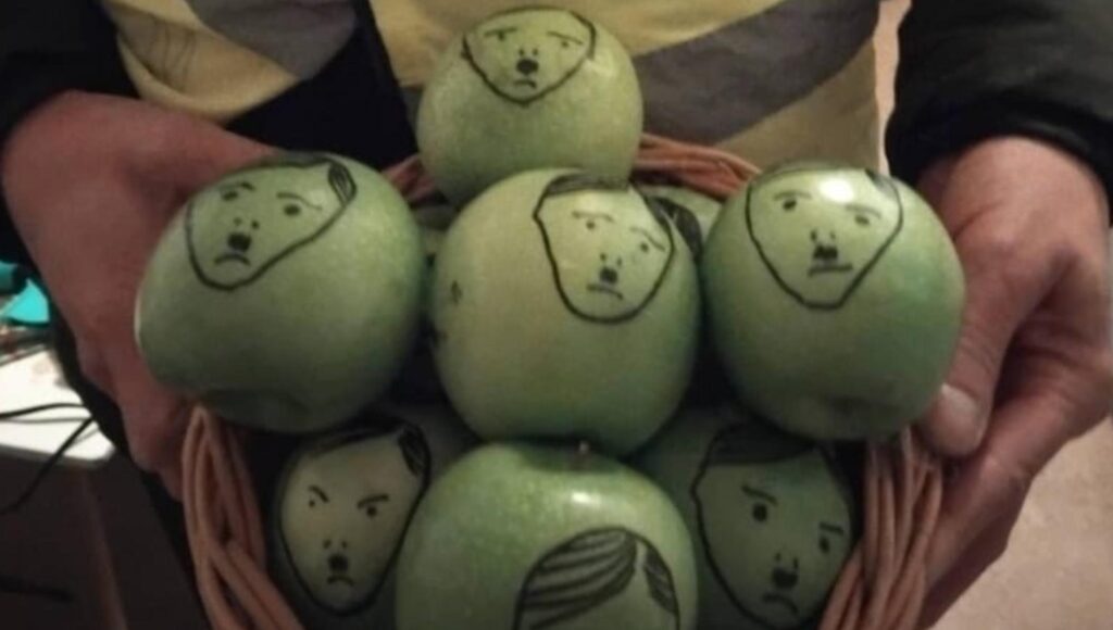 Gröna äpplen i en flätad korg med handritade ansikten av Hitler.