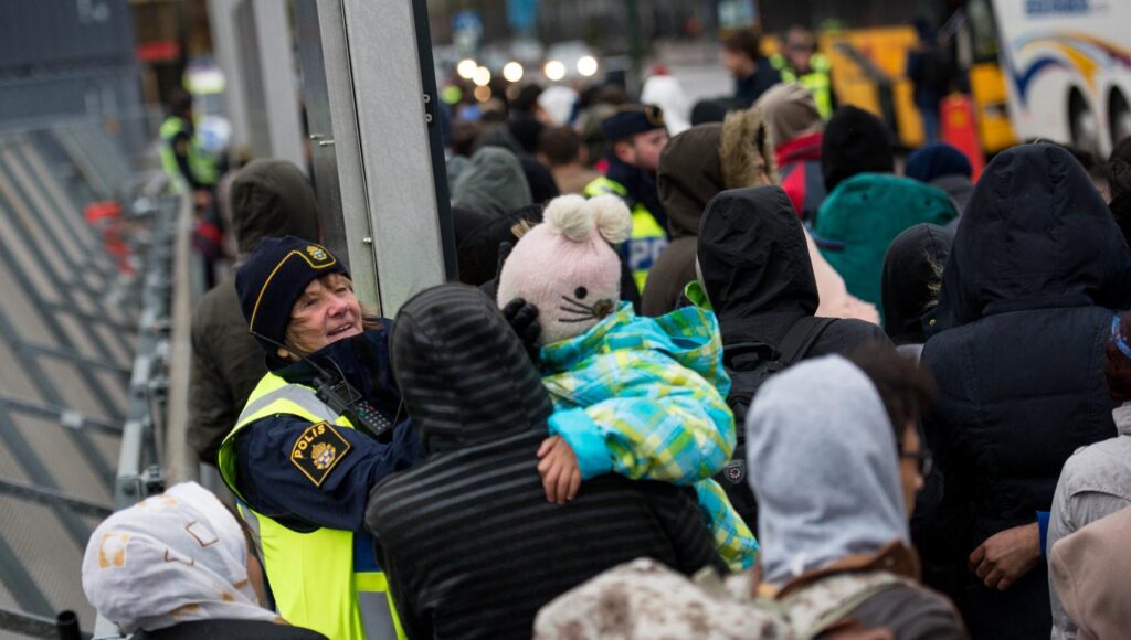 Svensk polis pratar med ett barn i mössa framför en stor folkmassa utomhus.