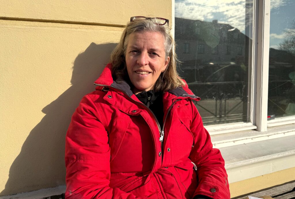 En kvinna i röd vinterjacka ler mot kameran i solljus utomhus