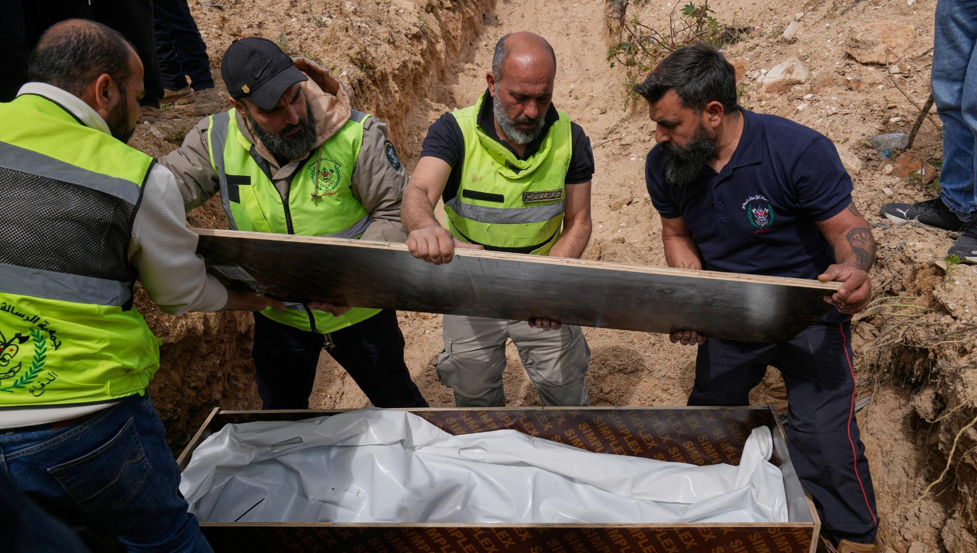 Civilförsvarspersonal i Libanon arbetar med att förbereda en begravning mitt under det pågående kriget mellan Israel och Hizbollah. Männen ses lyfta en träskiva över en kista täckt med vit plast i en provisorisk grav utomhus. Foto: Hussein Malla/TT