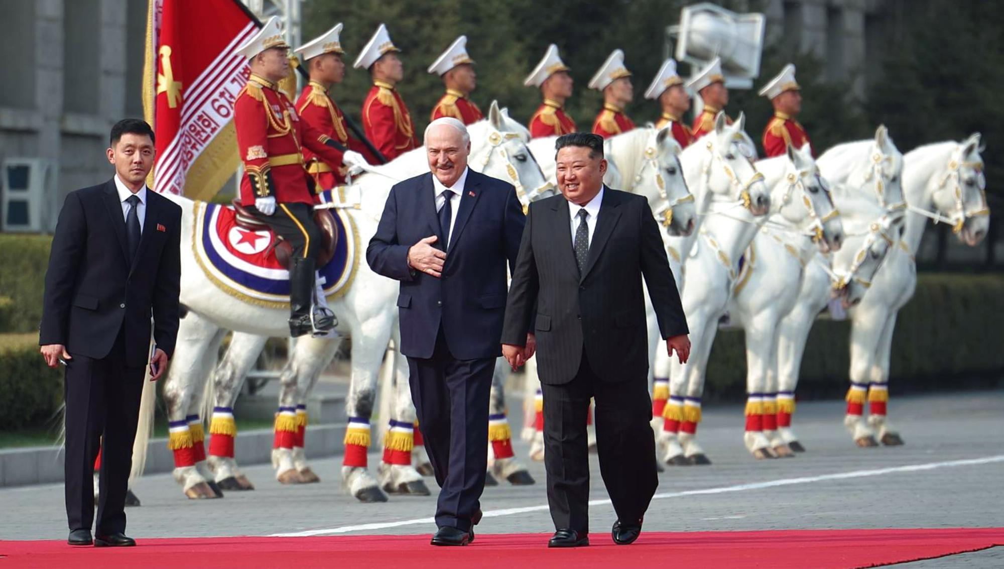 Alexander Lukashenko och Kim Jong Un promenerar tillsammans på en röd matta under ett officiellt statsbesök i Nordkorea. I bakgrunden syns en ryttarvakt med soldater i ceremoniella uniformer på vita hästar. Foto: TT