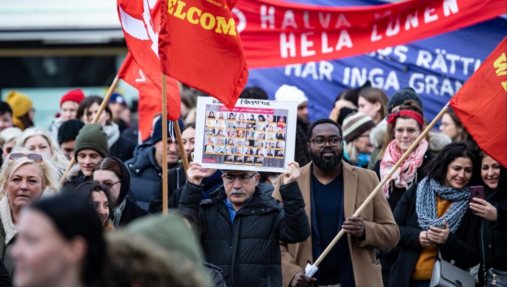 Momodou Malcolm Jallow och andra demonstranter i Malmö bär fanor och ett plakat med foton på kvinnor.