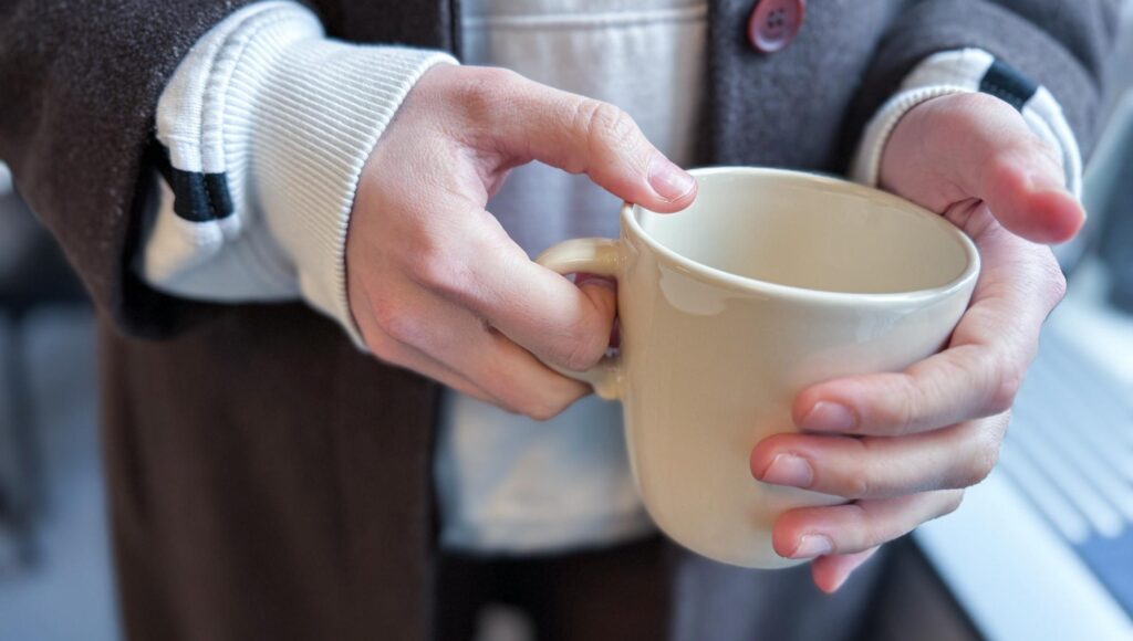 Närbild på en persons händer som håller i en beige mugg