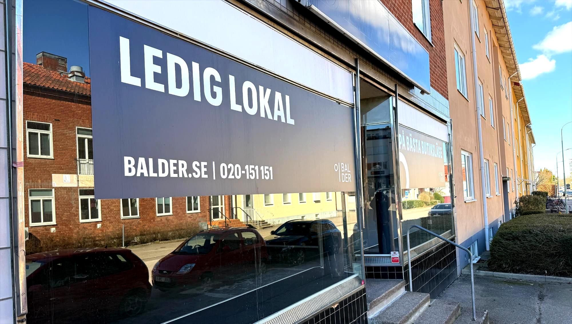 En butikslokal står tom i bottenvåningen på ett hyreshus med en stor skylt från fastighetsbolaget Balder som annonserar efter nya hyresgäster.