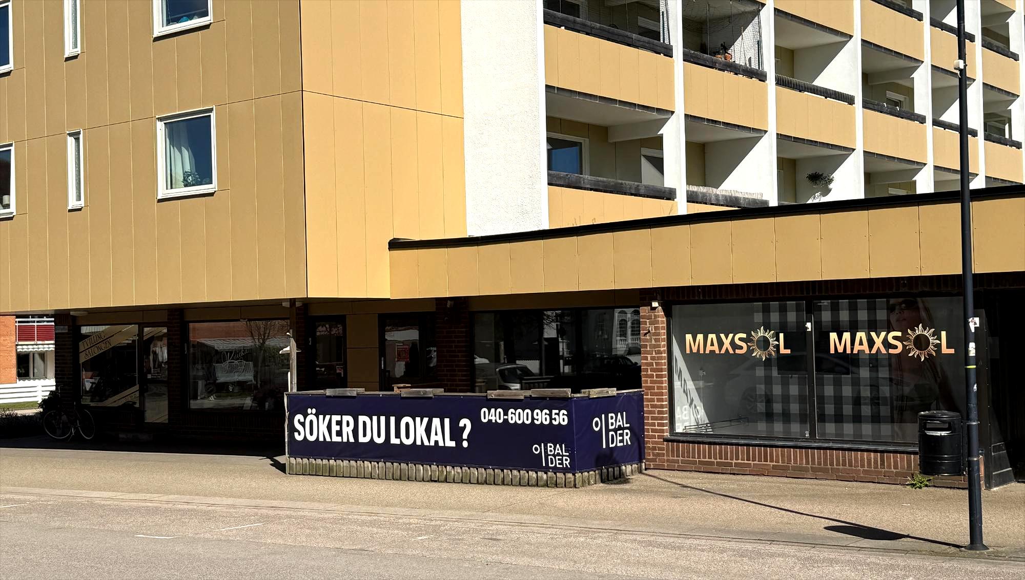 En skylt från fastighetsbolaget Balder annonserar efter hyresgäster till en ledig lokal på bottenplan i ett gult flerbostadshus i Åstorp.