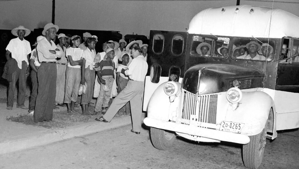 Svartvitt foto på en grupp människor som väntar vid en gammal buss under dygnets mörka timmar