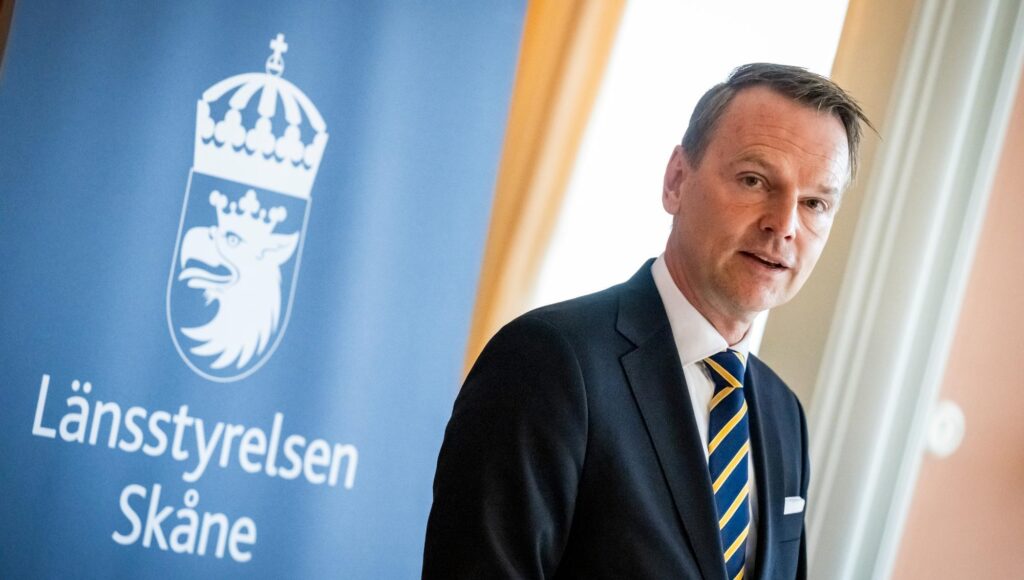 En man i mörk kostym och gulblå slips står framför Länsstyrelsen Skånes logotyp.