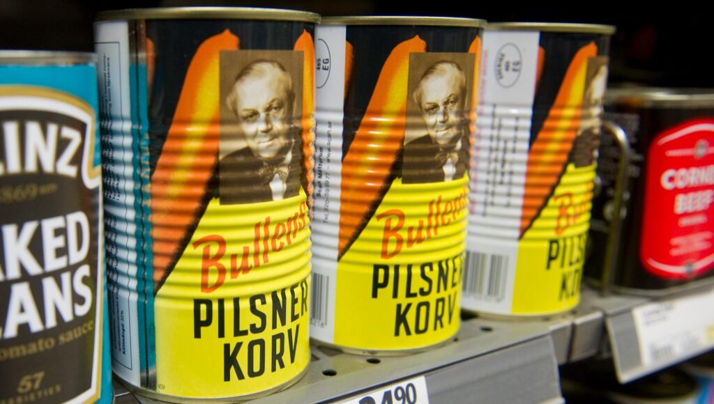 Konservburkar med pilsnerkorv och vita bönor står på rad i en butikshylla.