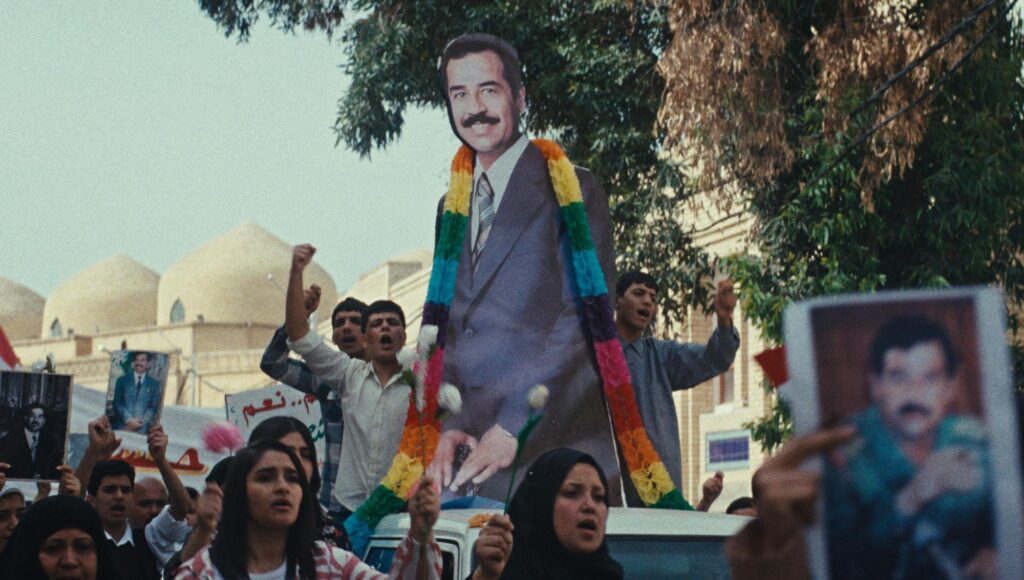 Folkmassa demonstrerar med en stor pappfigur av Saddam Hussein prydd med färgglada girlanger.