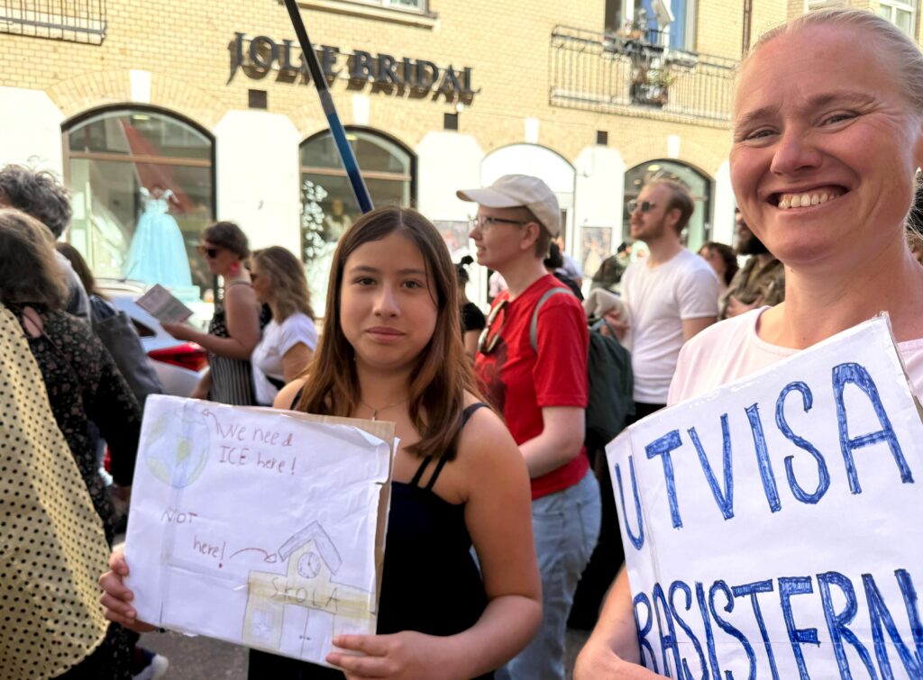 Två kvinnor i en folksamling håller upp handgjorda plakat med politiska budskap mot rasism.