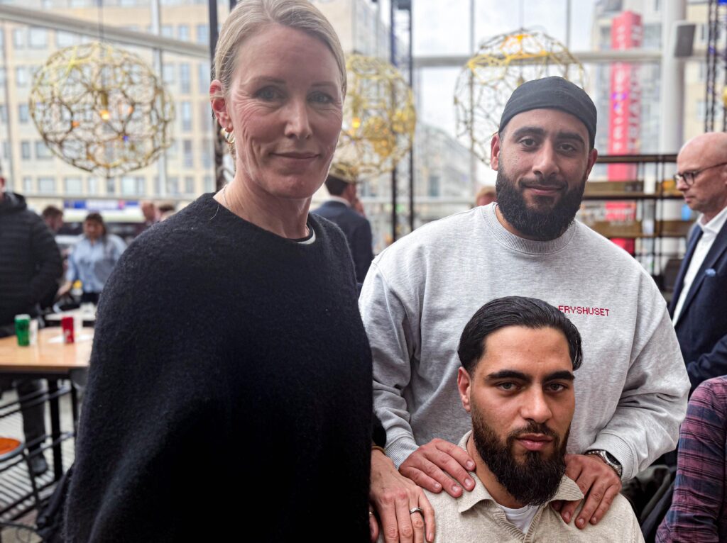 En kvinna och två män med skägg poserar tillsammans i en ljus lokal med stora fönster mot Triangeln.