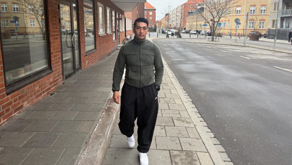 En man i träningskläder promenerar längs en trottoar med tegelhus i bakgrunden