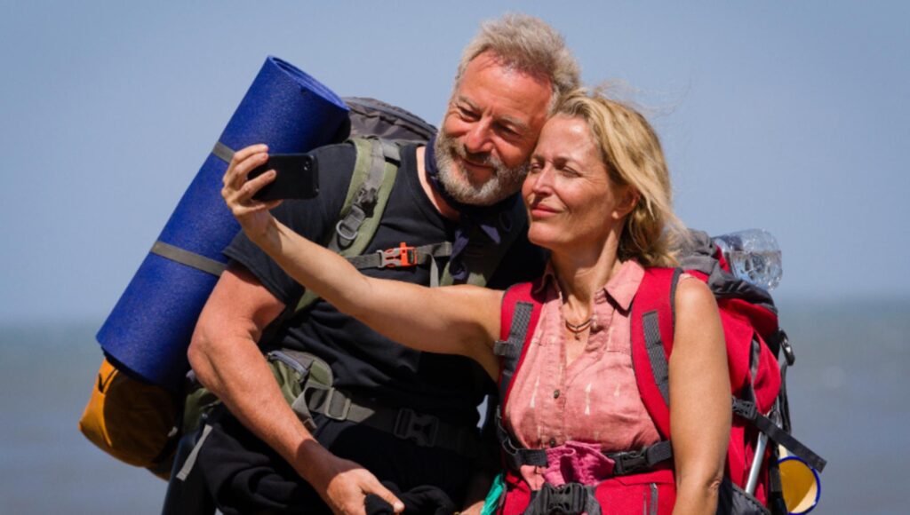 En kvinna och en man med stora ryggsäckar tar en selfie utomhus i solljus.