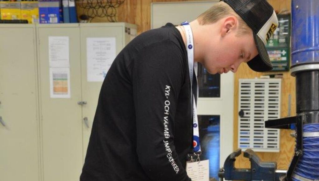 Ung man i keps och svart långärmad tröja arbetar i en verkstadsmiljö.