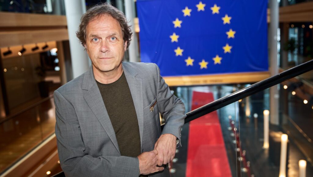Man i grå kavaj står vid ett räcke framför EU-flaggan och en röd matta.