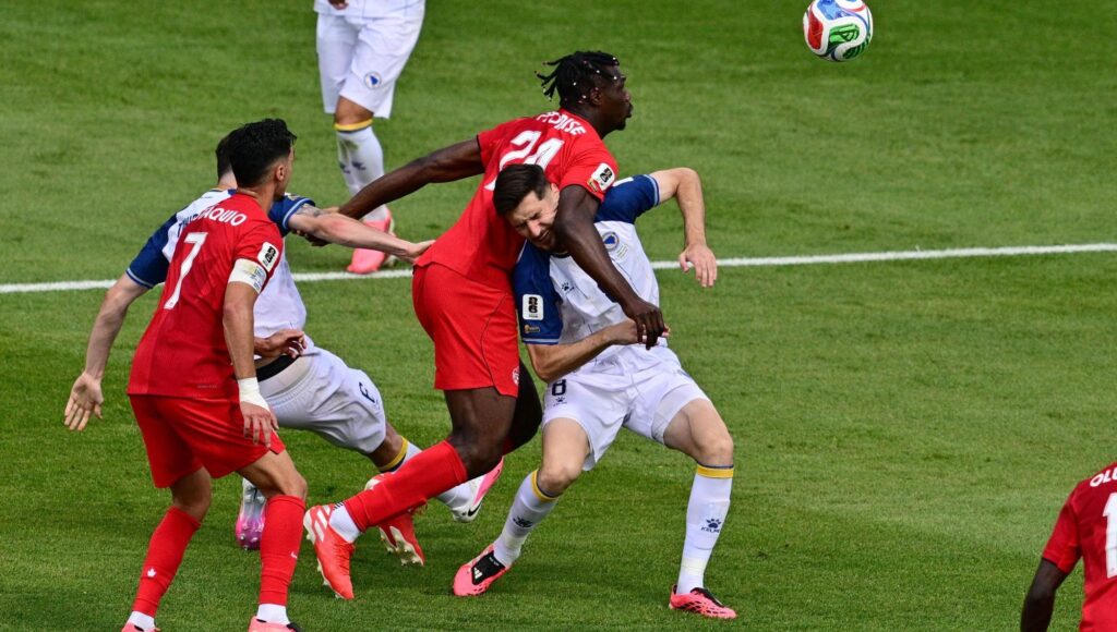 Fotbollsspelare i rött och vitt kämpar om bollen i en närkontakt på en gräsplan.