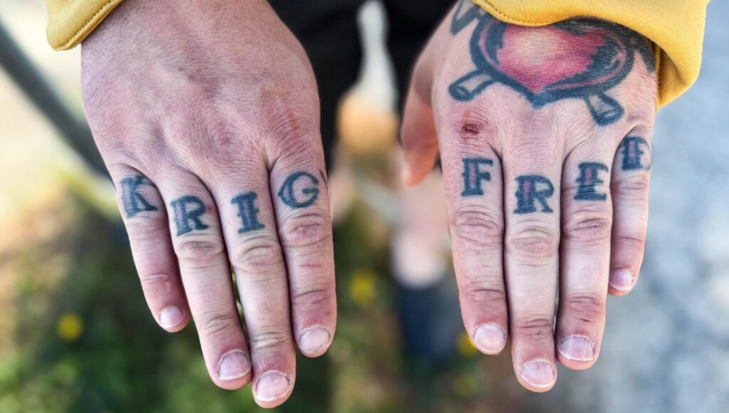 Närbild på två händer med tatueringarna KRIG och FRED på fingrarna och ett hjärta på handryggen.