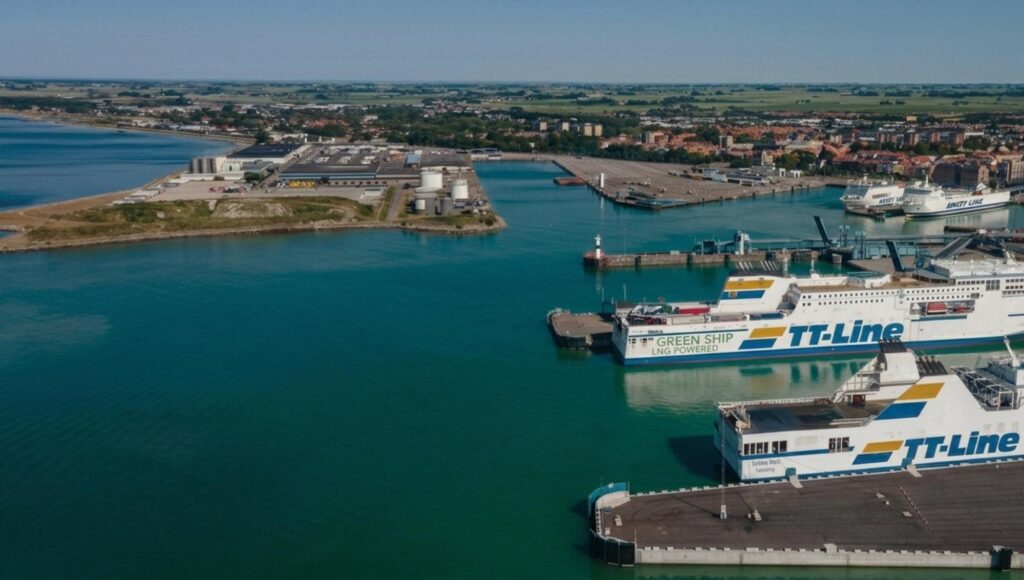 Flygbild över Trelleborgs hamn med flera stora TT-Line-färjor förtöjda vid kajer i turkost vatten.