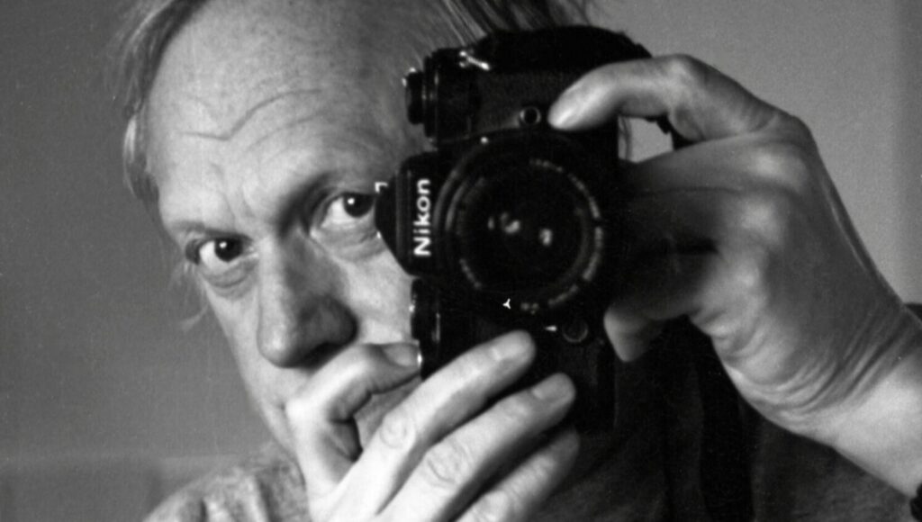 Svartvitt närporträtt av en man som håller en Nikon-kamera framför sitt ena öga.