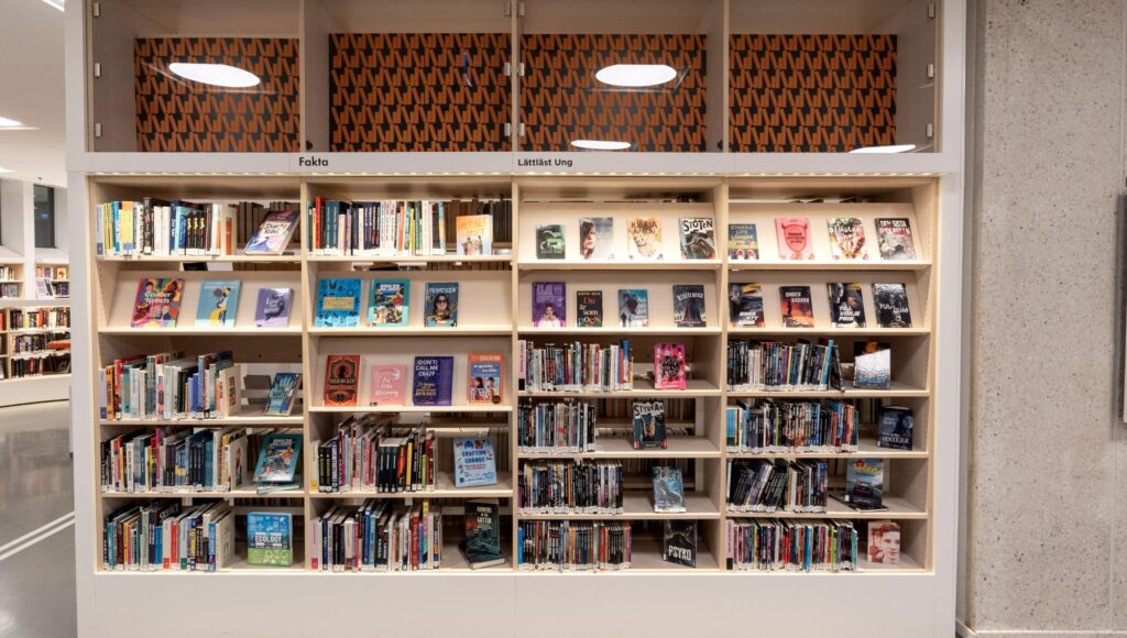 Välfyllda bokhyllor på ett bibliotek med sektioner för fakta och lättläst litteratur för unga.