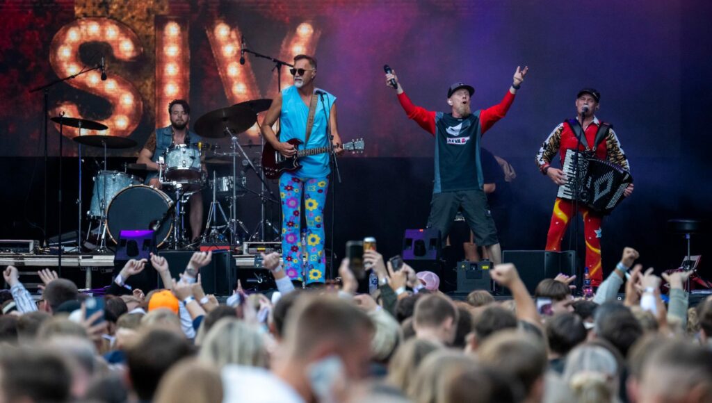 Bandet Joddla med Siv i färgglada kläder på scen framför en jublande publik under en utomhusfestival.