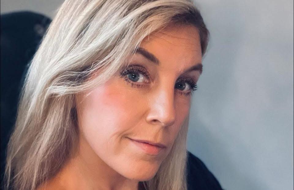 Närbild på en kvinna med långt ljust hår som tittar in i kameran mot en ljus bakgrund.
