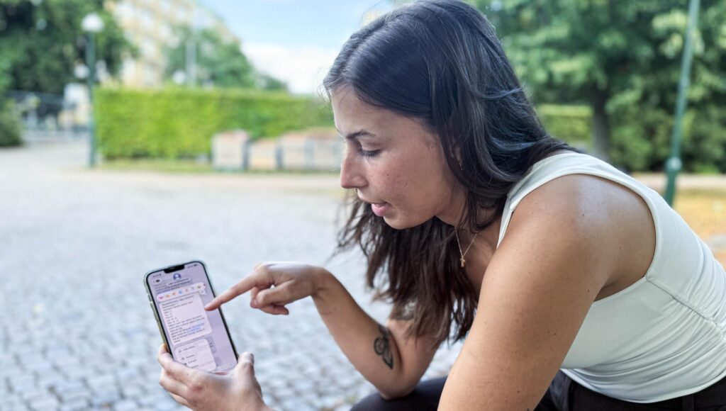 En kvinna i 20-årsåldern pekar på ett textmeddelande i sin mobiltelefon utomhus.