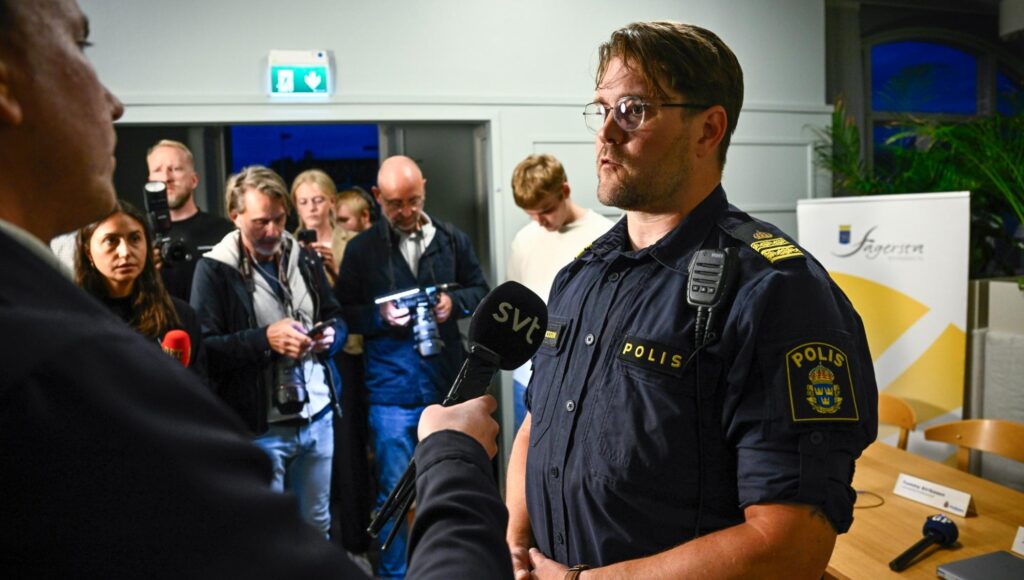 En polis i uniform intervjuas av en reporter med SVT-mikrofon framför ett medieuppbåd.