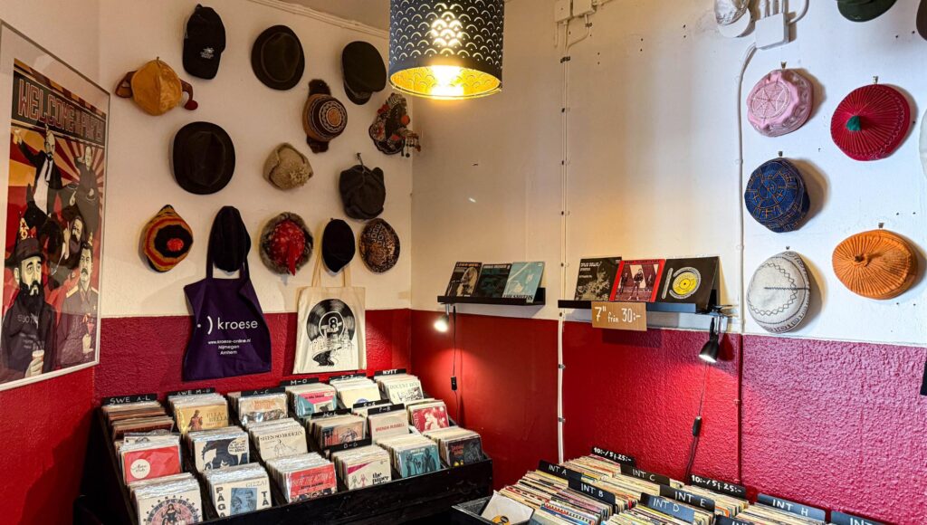 Interiör i skivbutik med backar av vinylskivor, röda väggar och ett stort urval av hattar upphängda på väggen.