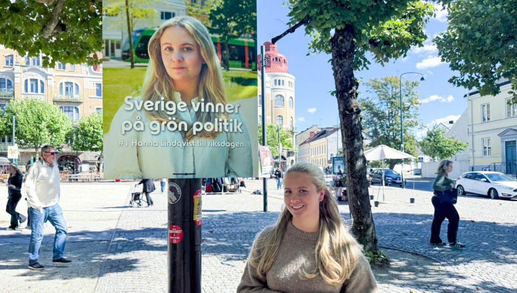 En ung kvinna ler framför en valaffisch med sitt eget ansikte på ett soligt torg.