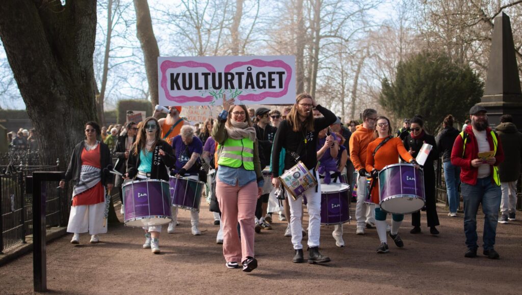 Folkmassa med trummor och en skylt med texten Kulturtåget går på en parkväg.