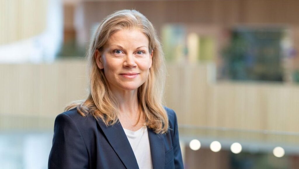 Porträtt av kvinna i 40-årsåldern med blont hår iklädd blå kavaj mot suddig kontorsbakgrund